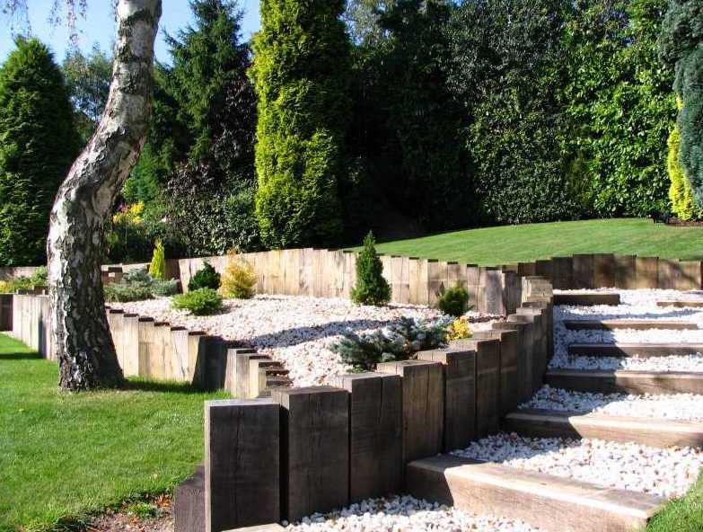 New oak railway sleepers are fixed vertically in concrete to create a create a curved retaining wall. Railwaysleepers.com